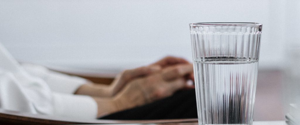 hands resting on a laptop with a glass of water in the foreground.